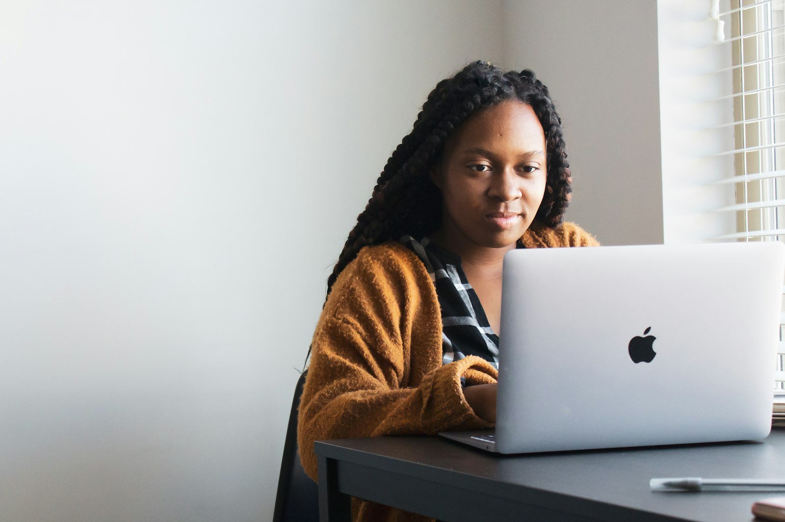Woman with braids working on a laptop by a window